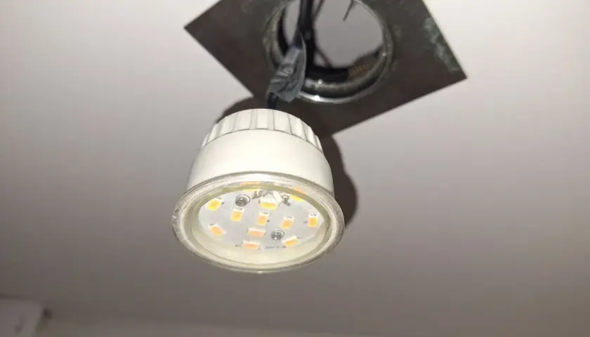 Wymiana żarówki LED GU10: widoczna jest nowa żarówka LED GU10 wisząca obok oprawy sufitowej, gotowa do montażu.