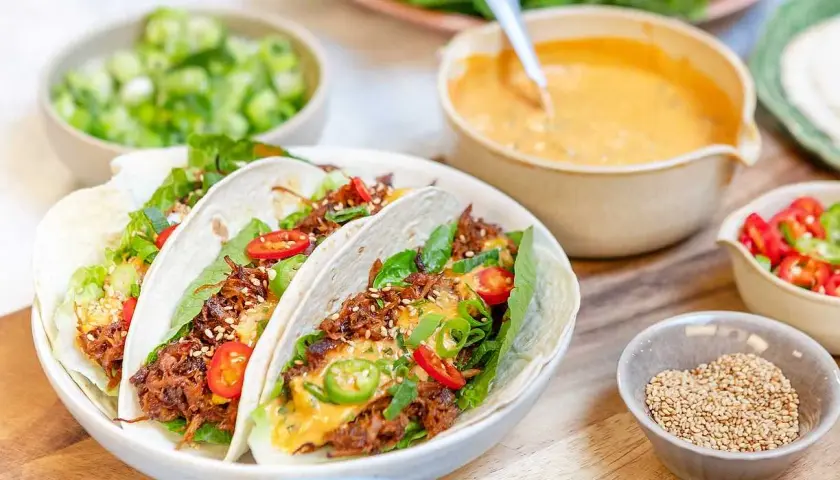 Tacos med koreansk pulled pork, toppade med sallad, chili och sesamfrön. Serveras med en krämig sås och färska grönsaker.