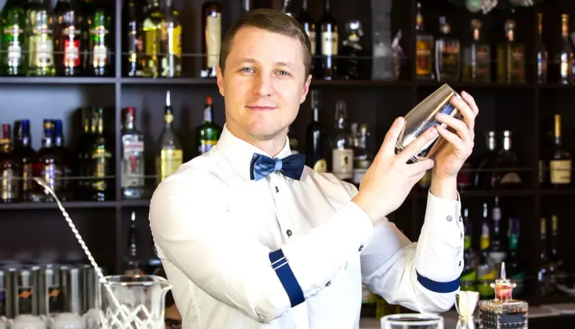 Uśmiechnięty barman z shakerem w dłoniach, za nim półki z alkoholem. Zastanawiasz się, ile zarabia barman za granicą?
