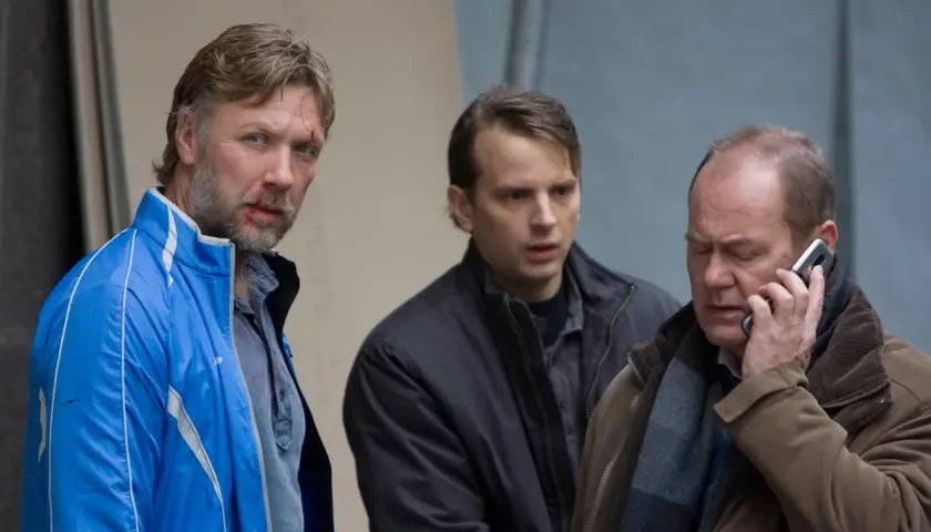 Tomas Fryk, med blodfläckar i ansiktet, står med två andra män. En pratar i telefon.