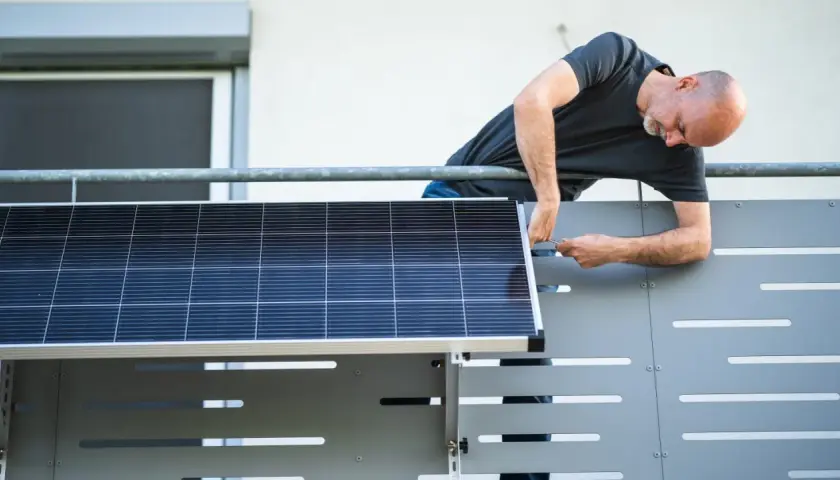 Mann montiert Solarmodul auf einem Balkongeländer.