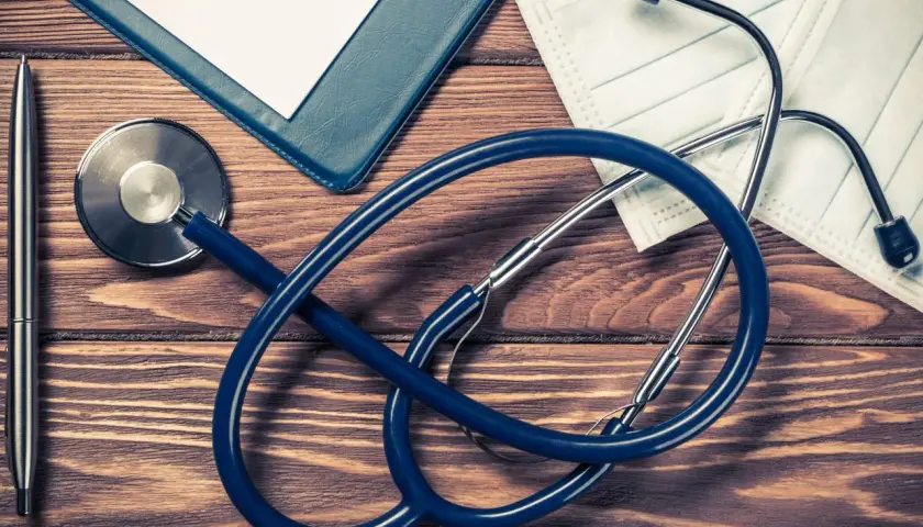 Stetoscopio, penna, cartella e mascherina su tavolo di legno. Preparativi per aprire studio medico in appartamento.
