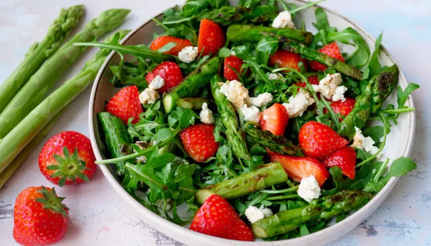 Frischer Spargelsalat mit Erdbeeren und Rucola, garniert mit zerbröseltem Käse.