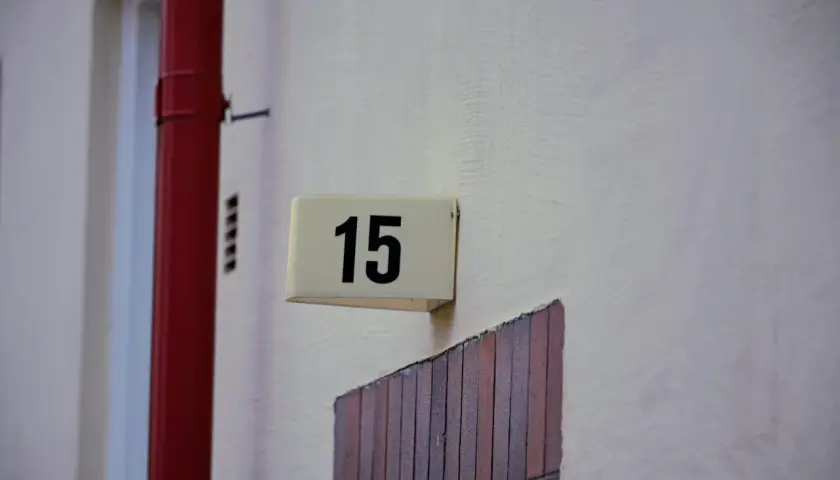 Tabliczka z numerem 15 na ścianie, obok czerwonej rury. Idealne wskazanie adresu dla najmu okazjonalnego.