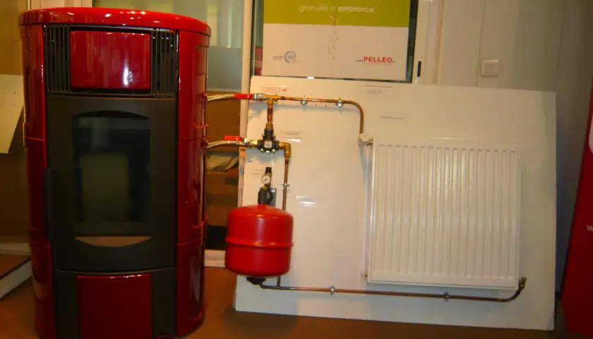 Poêle à granulé hydro rouge connecté à un radiateur blanc. Le système de chauffage est prêt.