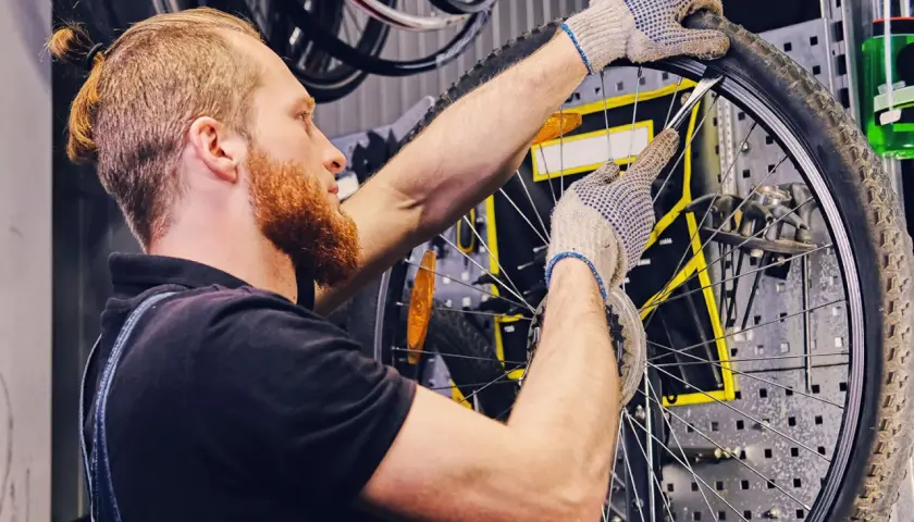 Mechanik w rękawiczkach naprawia **detkę** w rowerze, używając łyżki do opon.