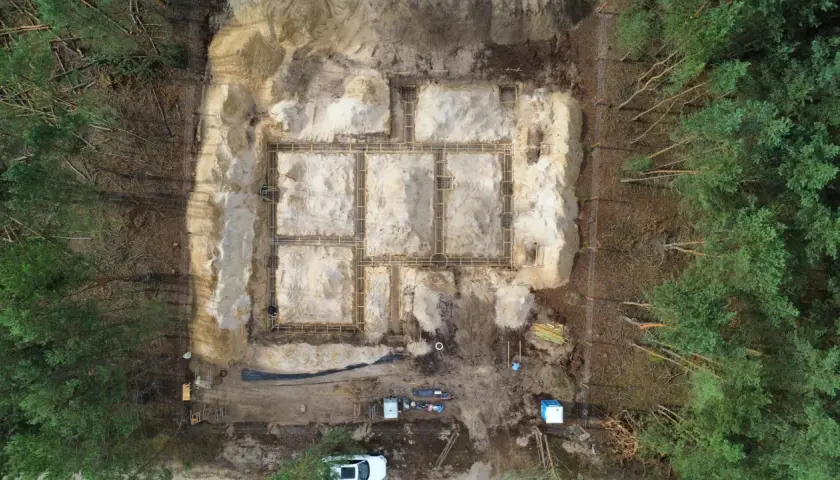 Budowa fundamentów domu w lesie. Widać zbrojenie i szalunki. W tle drzewa. To etap prac poprzedzający badania geotechniczne gruntu.
