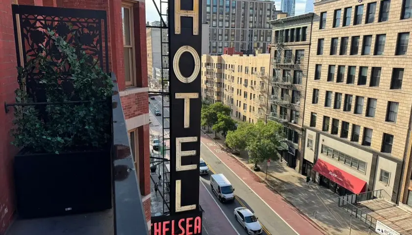 Neo-upplyst skylt för Chelsea Hotel, med en balkong med växter i förgrunden.