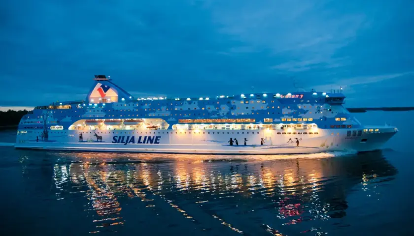 Prom Silja Line Galaxy płynie po wodzie o zmierzchu, odbijając światła w mroku. Podróż z Rygi do Helsinek zaczyna się!
