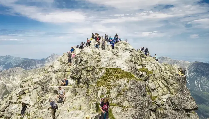 Tłum turystów na skalistym szczycie, najwyższy szczyt w Polsce, Rysy, podziwia panoramę Tatr.
