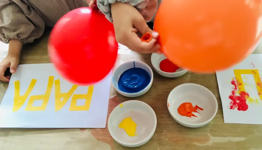Kinder malen mit Luftballons bunte Muster auf Papier. Rote und orange Luftballons werden in Farbe getaucht.