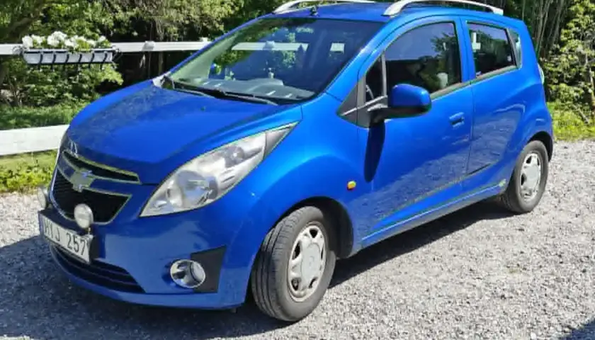 Blå Chevrolet Spark med extraljus, kanske ett problem med bilen? Parkerad på grusväg.