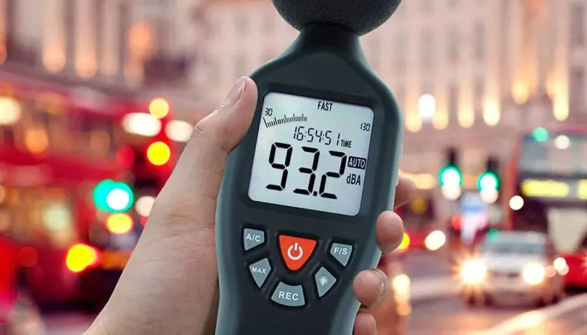 Mano sosteniendo un medidor de sonido para medir db en una calle ruidosa de la ciudad.