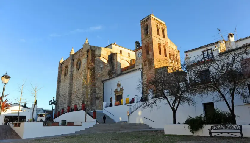 Iglesia de la Asunción en Cazalla de la Sierra, con su torre campanario y fachadas de piedra y cal bajo un cielo azul.