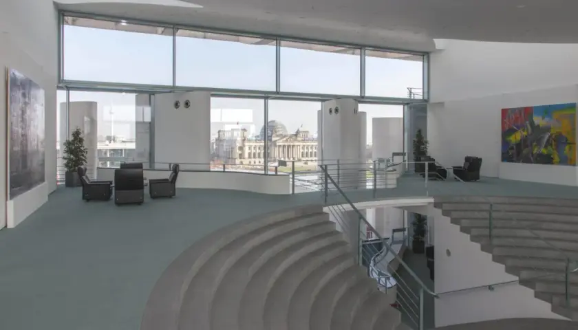 Modernes Foyer im Bundeskanzleramt mit Blick auf das Reichstagsgebäude. Sitzgruppen und eine geschwungene Treppe laden zum Verweilen ein.