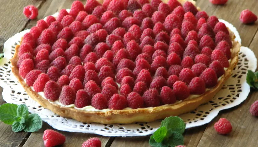 Pyszna tarta z malinami, udekorowana świeżymi listkami mięty. Idealna na letnie popołudnie.