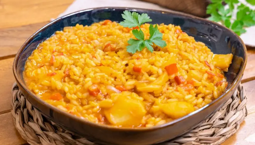 Un plato humeante de arroz con bacalao, adornado con perejil fresco, servido en un cuenco azul sobre una esterilla de mimbre.