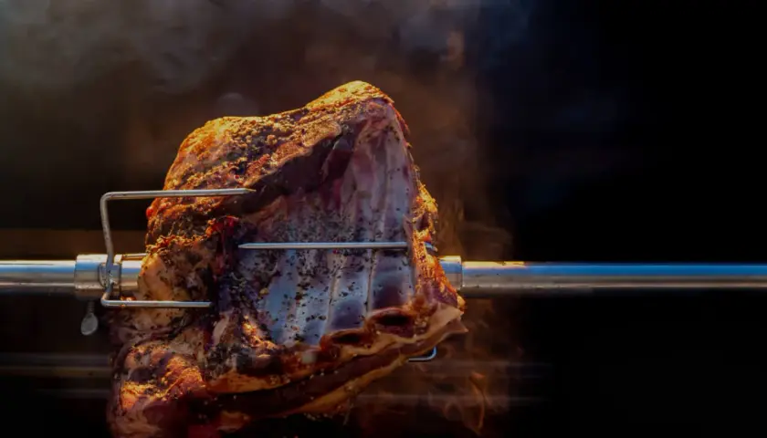 Un morceau de viande assaisonné tourne lentement sur une broche, dégageant une fumée alléchante. La cuisson à la broche promet un délice savoureux.