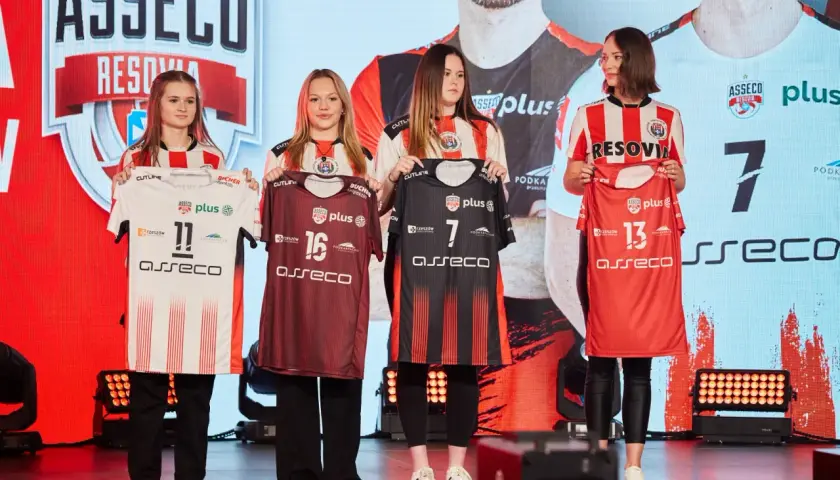 Cztery młode kobiety prezentują koszulki siatkarskie drużyny Asseco Resovia. Dwie w białych, dwie w ciemnych strojach.