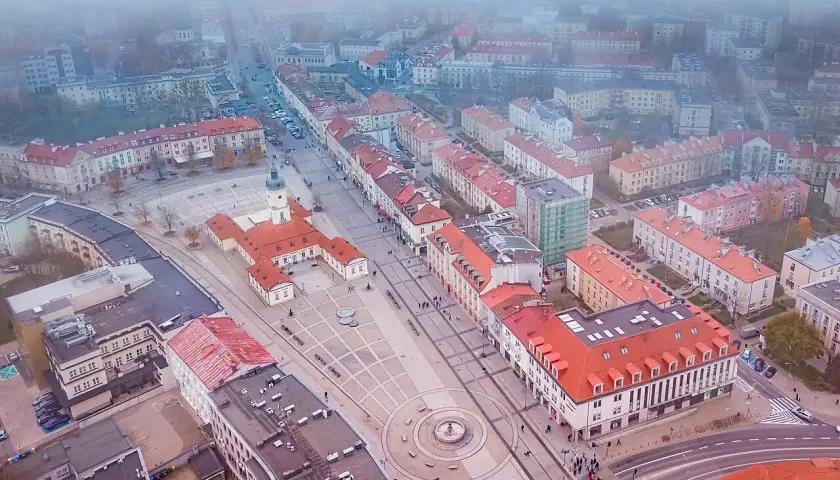 Widok z lotu ptaka na rynek Kościuszki w Białymstoku, otoczony kamienicami i budynkiem ratusza.