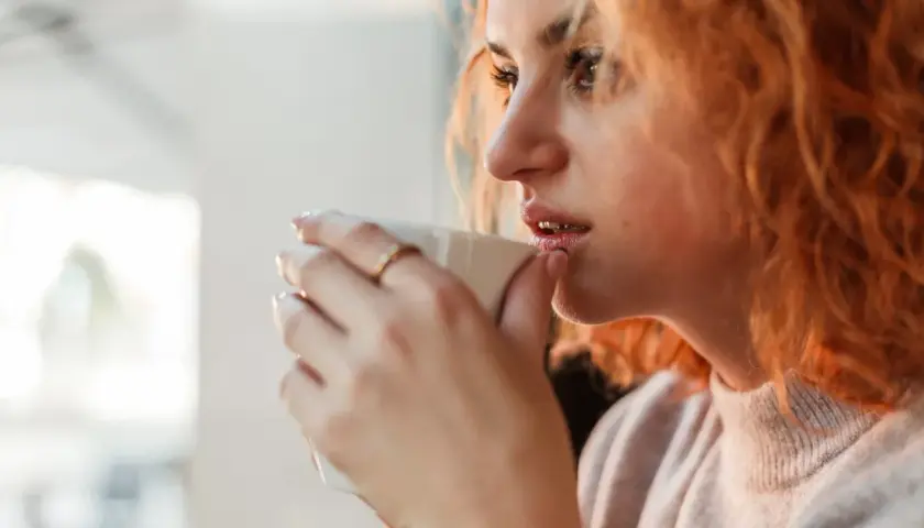 Ruda kobieta pije kawę, czując jak 1000 mg kofeiny na raz pobudza jej zmysły.
