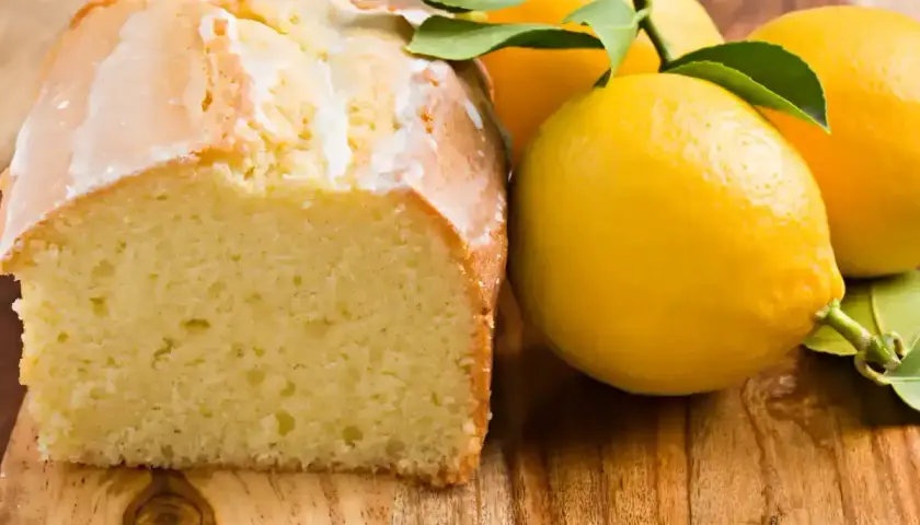 Un délicieux gâteau citron, avec un glaçage blanc et des citrons frais sur une planche en bois.