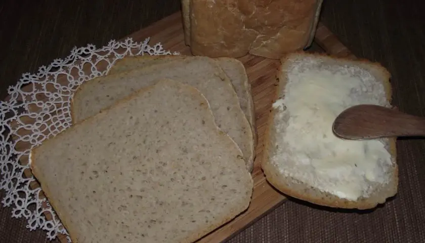 Chleb pszenno żytni na zakwasie, pokrojony w kromki. Jedna kromka posmarowana masłem, obok leżą kolejne.