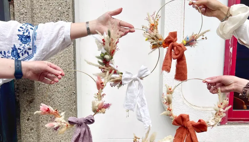 Des mains créatives assemblent des couronnes de fleurs séchées lors d'un atelier EVJF. Ambiance bohème et festive.