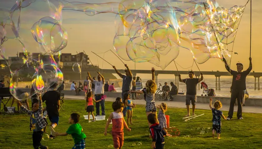 Un compleanno alternativo per bambini con bolle giganti al tramonto. Bambini e adulti si divertono a creare enormi bolle iridescenti sulla costa.
