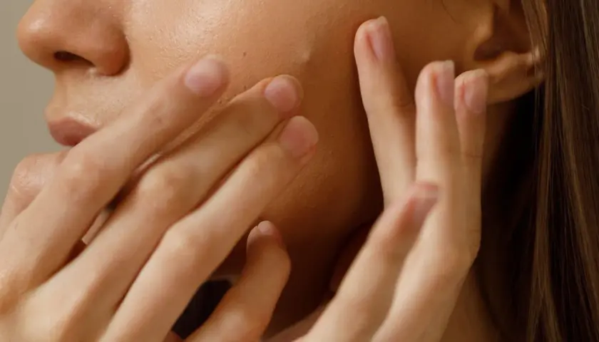Gros plan sur une peau claire avec un petit bouton sur le visage, touché par des doigts délicats.