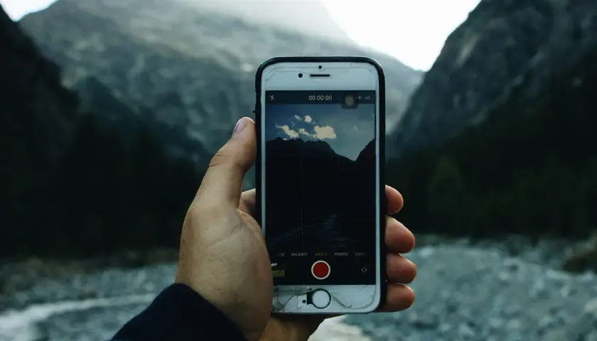Ręka trzyma telefon z otwartą aplikacją aparatu, gotową do robienia zdjęć górskiego krajobrazu.