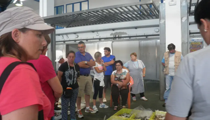 Gente en un mercado, con una lonja de muros al fondo.