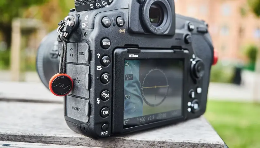 Nikon D850 test w plenerze. Aparat leży na drewnianym stole, w tle zieleń i budynek.
