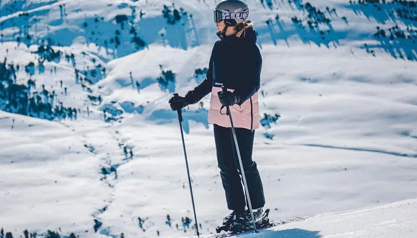 Narciarka w kasku i goglach stoi na stoku narciarskim z kijkami.
