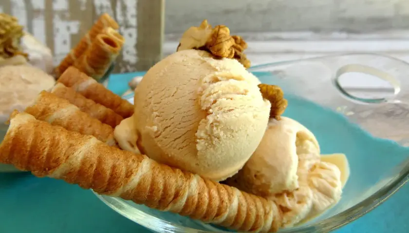 Delicioso helado de dulce de leche con barquillos crujientes y nueces, servido en un cuenco de vidrio sobre un plato turquesa.