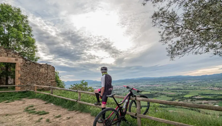 Ciclista descansa junto a su bici en ruinas de coll sa cabra, contemplando el valle.