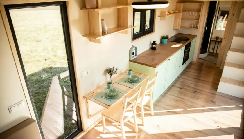 Gemütliches tiny house innen mit Esstisch, Küche und Blick ins Grüne.