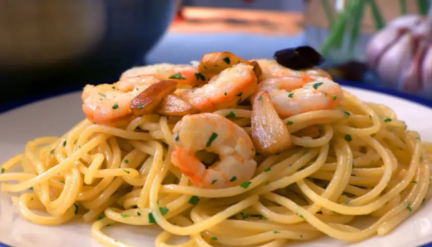 Espaguetis al ajillo con gambas, ajo laminado y perejil picado, servidos en un plato blanco.