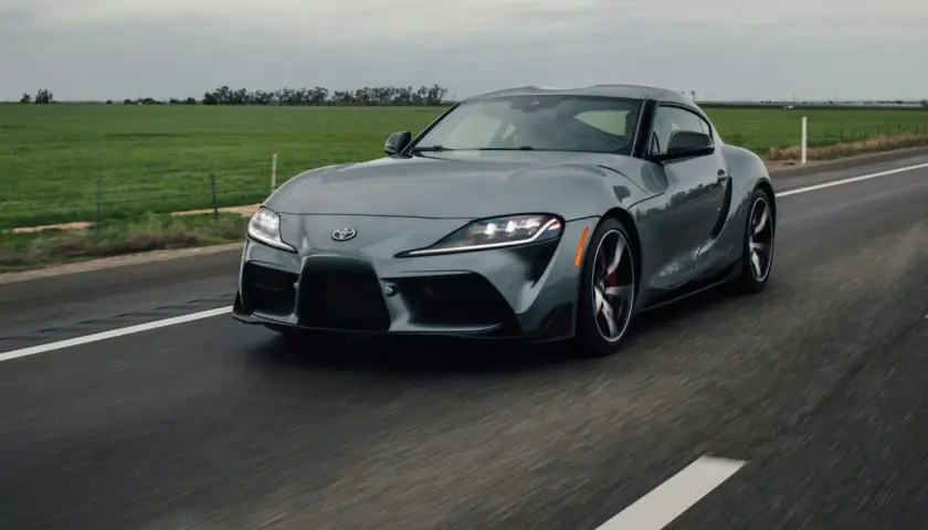 Szare auto sportowe jedzie po drodze. Ciemne felgi świetnie komponują się z nadwoziem, odpowiadając na pytanie: jaki kolor felg do srebrnego auta?