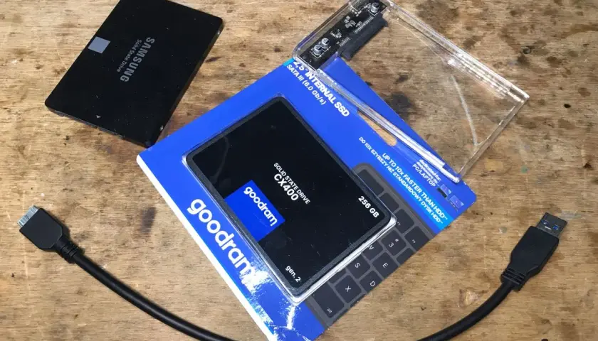 Dwa dyski SSD, jeden Samsung, drugi Goodram CX400 256 GB, obok obudowa na dysk i kable SATA.