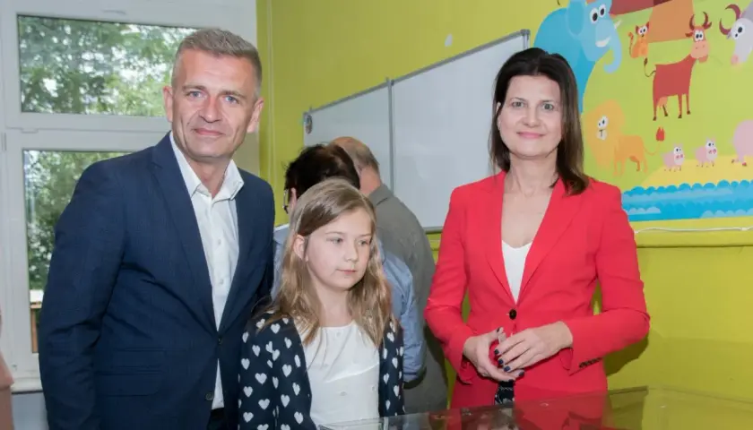 Bartosz Arłukowicz z córką i koleżanką na tle kolorowej ściany z bajkowymi zwierzątkami.