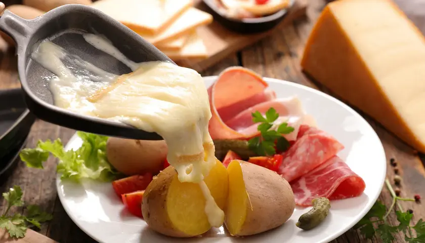 Le fromage à raclette fond sur des pommes de terre, prêt à être dégusté avec charcuterie et cornichons. Le temps de cuisson pomme de terre raclette est parfait.