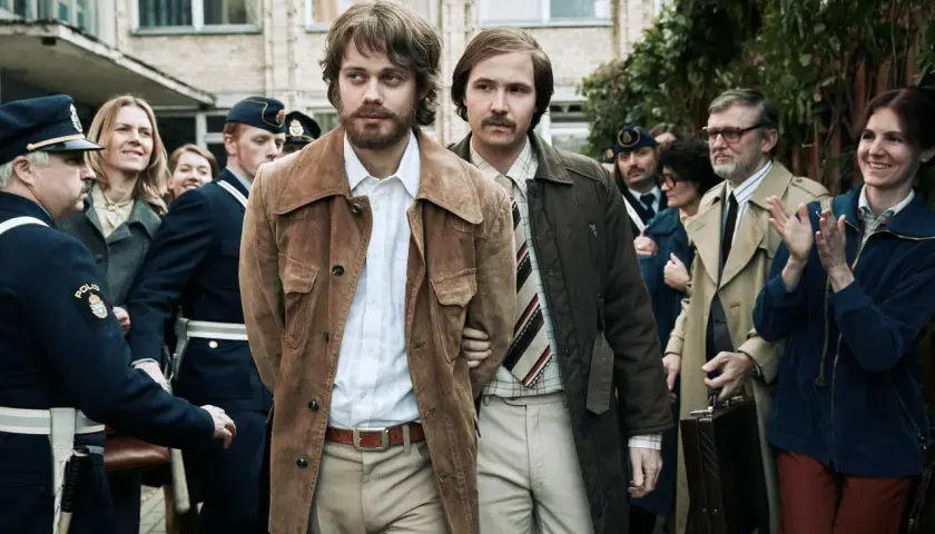 Två män förs till av poliser. En av dem, med bärnstensfärgad jacka, är Clark Olofsson i den hyllade clark olofsson serie.