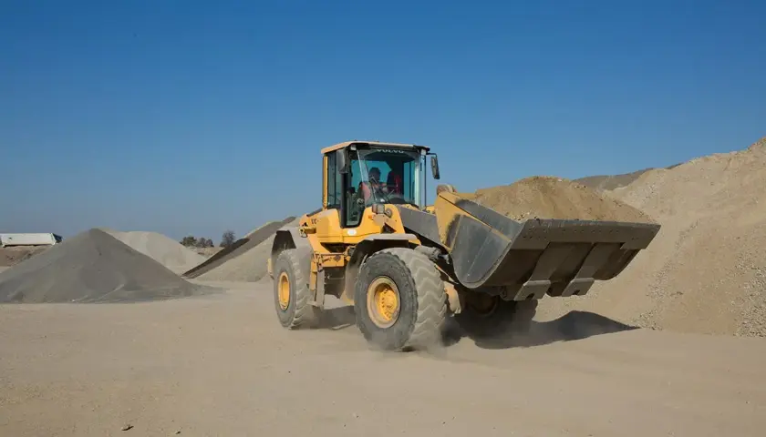 Żółta ładowarka Volvo z pełną łyżką ziemi. Posiadanie uprawnień na koparko ładowarki klasa 1 to klucz do obsługi takich maszyn.