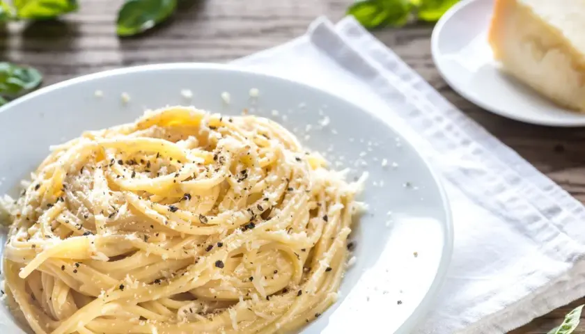 Szybki obiad z makaronem: spaghetti posypane parmezanem i pieprzem, obok kawałek sera i listki bazylii.