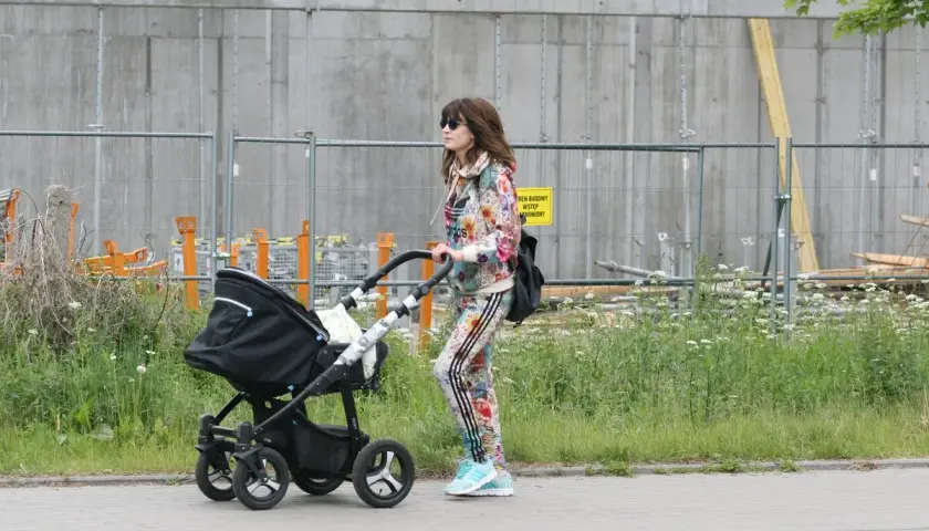 Kobieta w kolorowym dresie prowadzi czarny wózek dziecięcy.