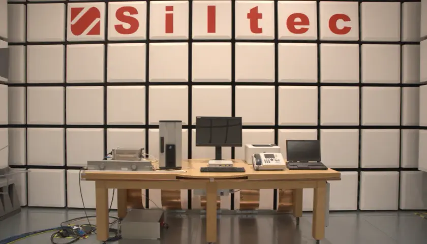 Laboratorium testowe z urządzeniami elektronicznymi i logo "Siltec". W tle ściana z paneli akustycznych, chroniąca przed zakłóceniami, jak podczas burzy (tempest).