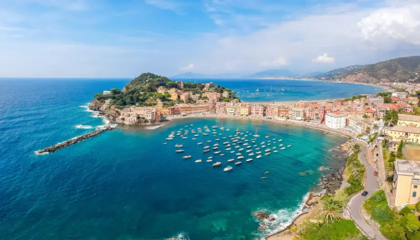 Vue aérienne de la baie de Sestri Levante, avec ses maisons colorées, sa plage et une multitude de bateaux dans les eaux turquoise.
