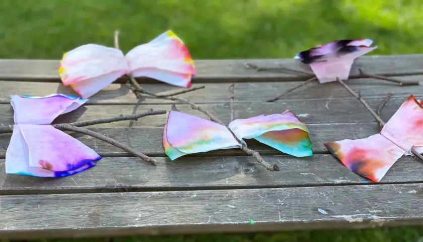 Bunte Schmetterlinge aus Kaffeefiltern, die Kinder leicht selber machen können, sitzen auf einem Holzbrett.