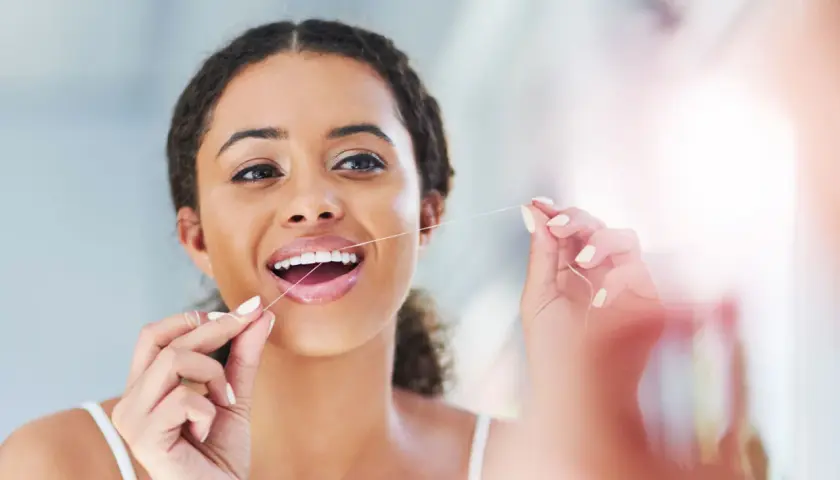 Donna sorridente usa il filo interdentale, un gesto quotidiano per un sorriso sano. Quante volte usare il filo interdentale? Almeno una volta al giorno.